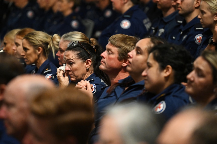 A large group of paramedics at a funeral, many of whom are crying.