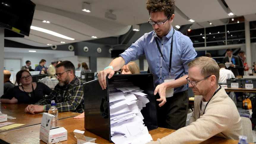 A box full of ballots is turned on its side to be counted as two men preside over it.