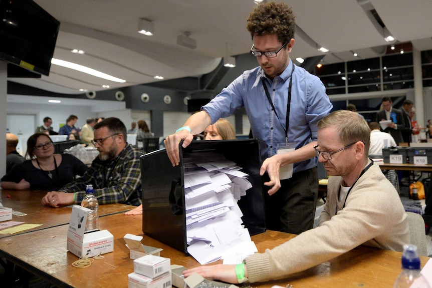 A box full of ballots is turned on its side to be counted as two men preside over it.