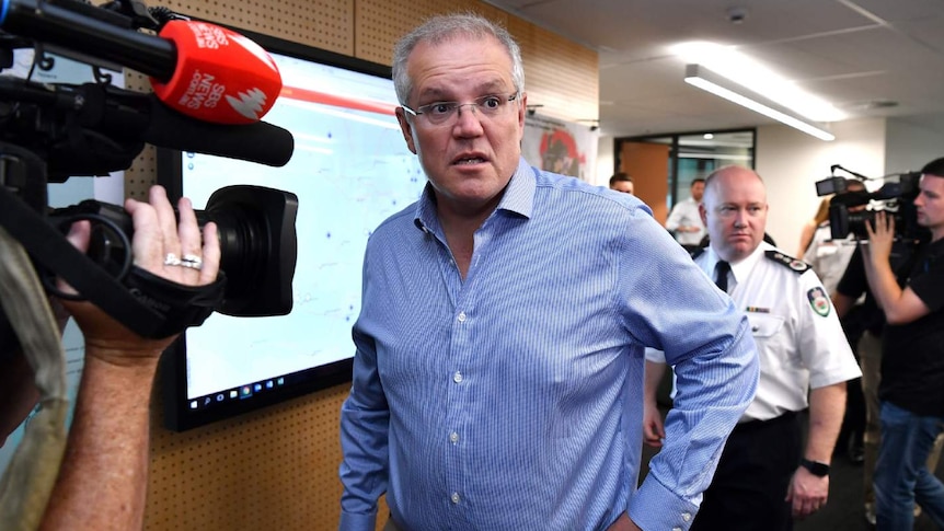 Scott Morrison, wearing a blue shirt, walks in front of cameras.