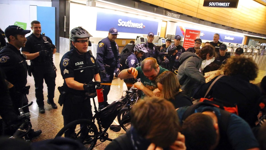 Seattle police use pepper spray and push the last group of protesters out of a Seattle airport terminal