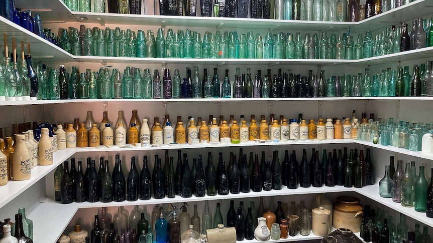 Walls covered in shelves which are filled with old bottles of various shapes and sizes with coloured glass and ceramic.