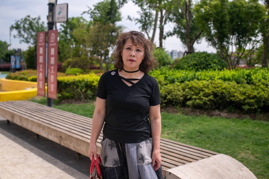 A middle aged woman stands in a Shanghai park.