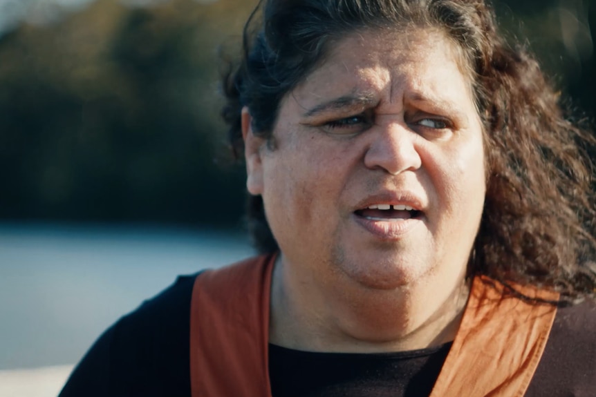 Close up of a woman singing with a lake in the background.