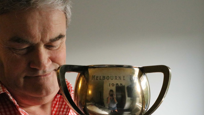 Middle aged man lovingly holds shiny cup with female photographer reflected