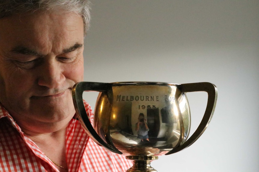 Middle aged man lovingly holds shiny cup with female photographer reflected