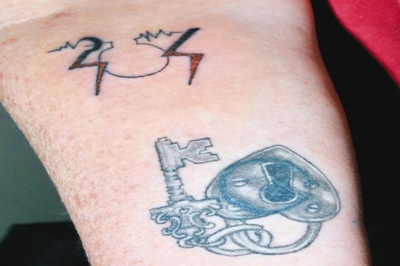 A close up of Trudi Lenon's arm showing two tattoos, an SOS in lightning bolts and an key and love heart lock.
