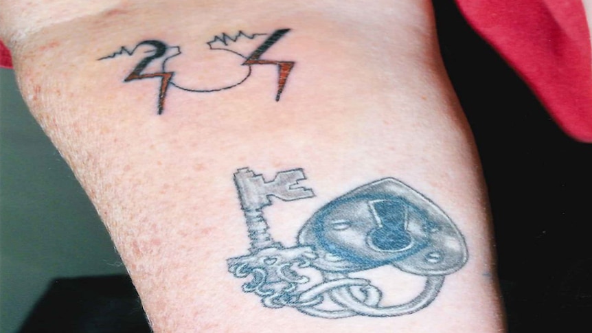 A close up of Trudi Lenon's arm showing two tattoos, an SOS in lightning bolts and an key and love heart lock.
