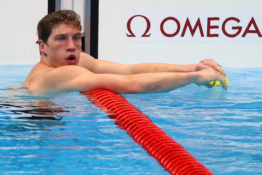 An Australian male swimmer gathers his breath as he leans over a lane rope.