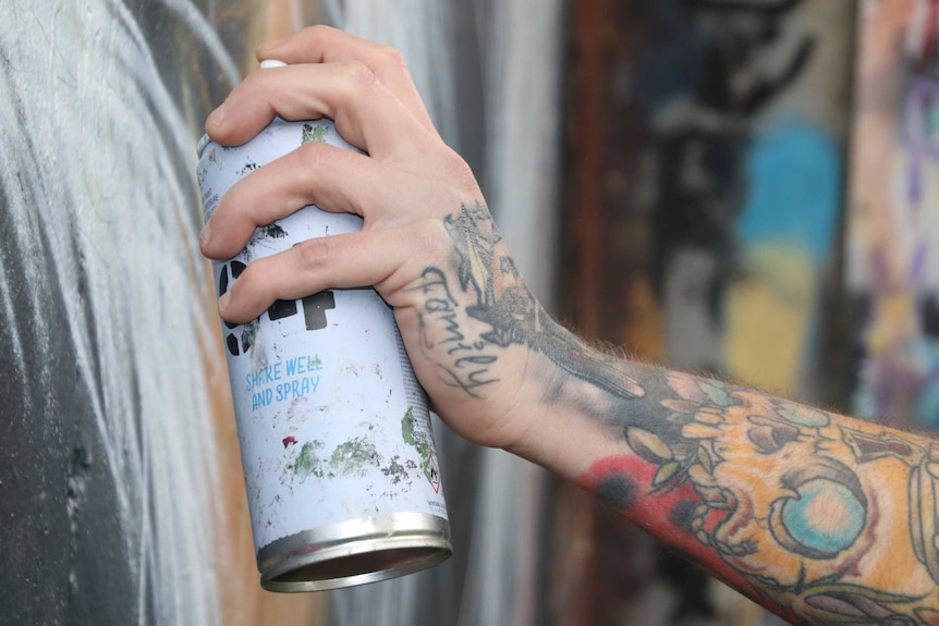 Hand of James Cowan holding an aerosol paint can and spray painting a mural.