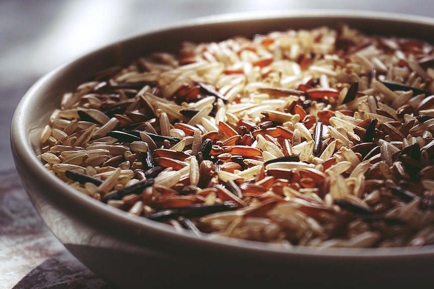 A close up photo of uncooked grains of coloured rice in a white ceramic bowl