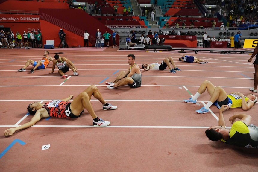 One athlete sits up while his fellow competitors lie exhausted on the track after a race.