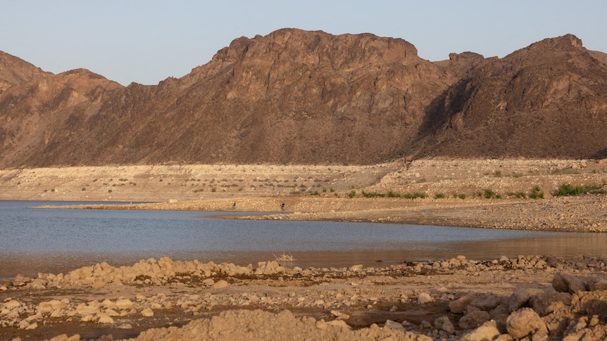 a dried-up lake with mostly brown dirt around a small section of brown-blue water, the sky above the landscape looks hazy