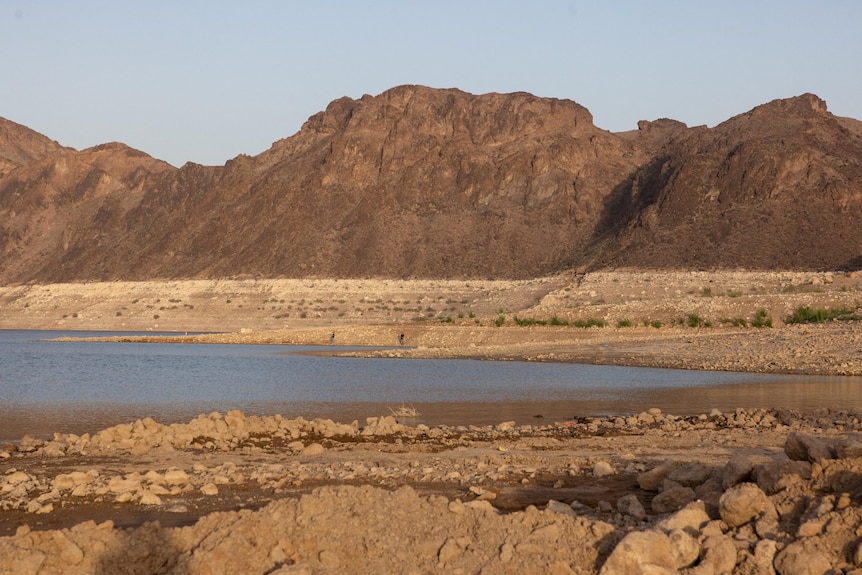 a dry lake with mostly brown dirt around a small section of blue-brown water, the sky above the landscape looks hazy