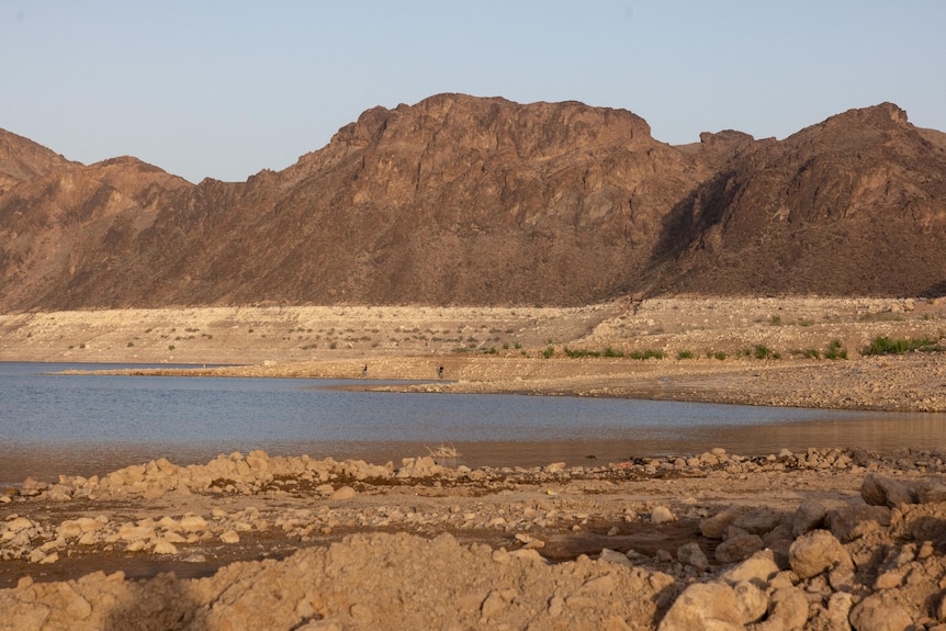 a dried-up lake with mostly brown dirt around a small section of brown-blue water, the sky above the landscape looks hazy