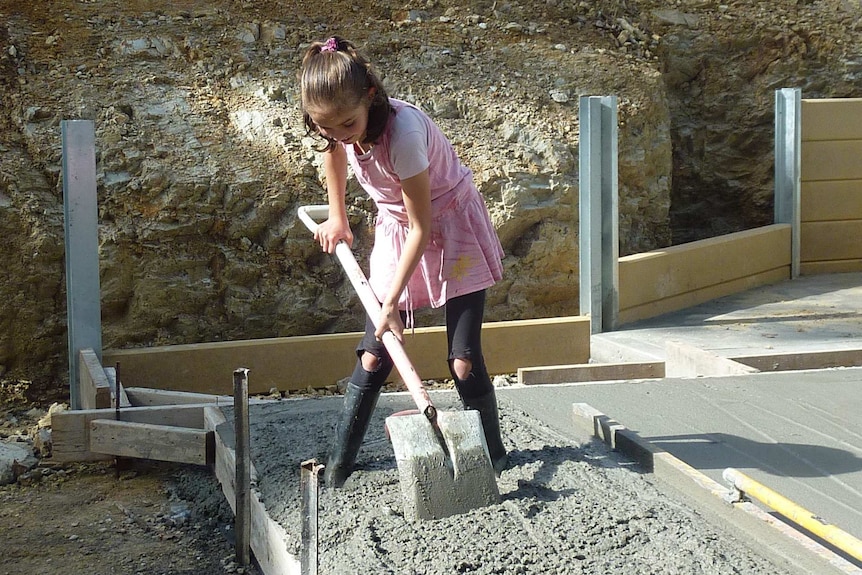A young girl digging wet concrete