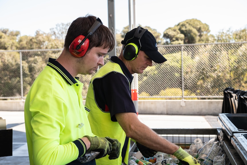 Two young men sort through a pile of containers.