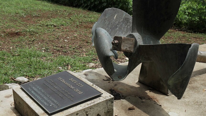 A monument overlooking a beach features a plaque and broken propeller