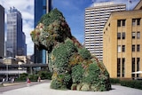 A our storey high sculpture of a puppy covered in flowers sits in front of a museum on Sydney Harbour.