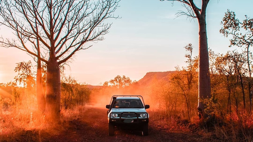 A four wheel drive travels down a dirt road as the sun sets in the background.