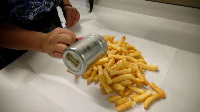 Person shakes salt onto hot chips sitting on wrapping paper