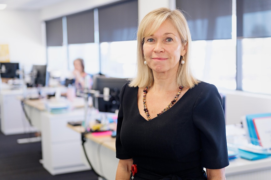 A woman wearing a black dress looks seriously at the camera and smiles.