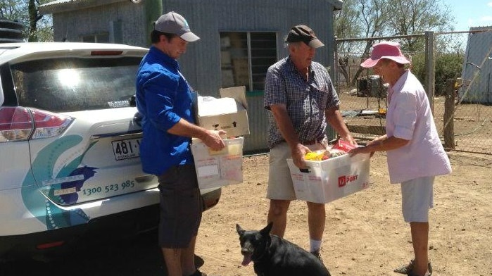 Three people and a dog surround the boot of a car as donated grocery items are handed over