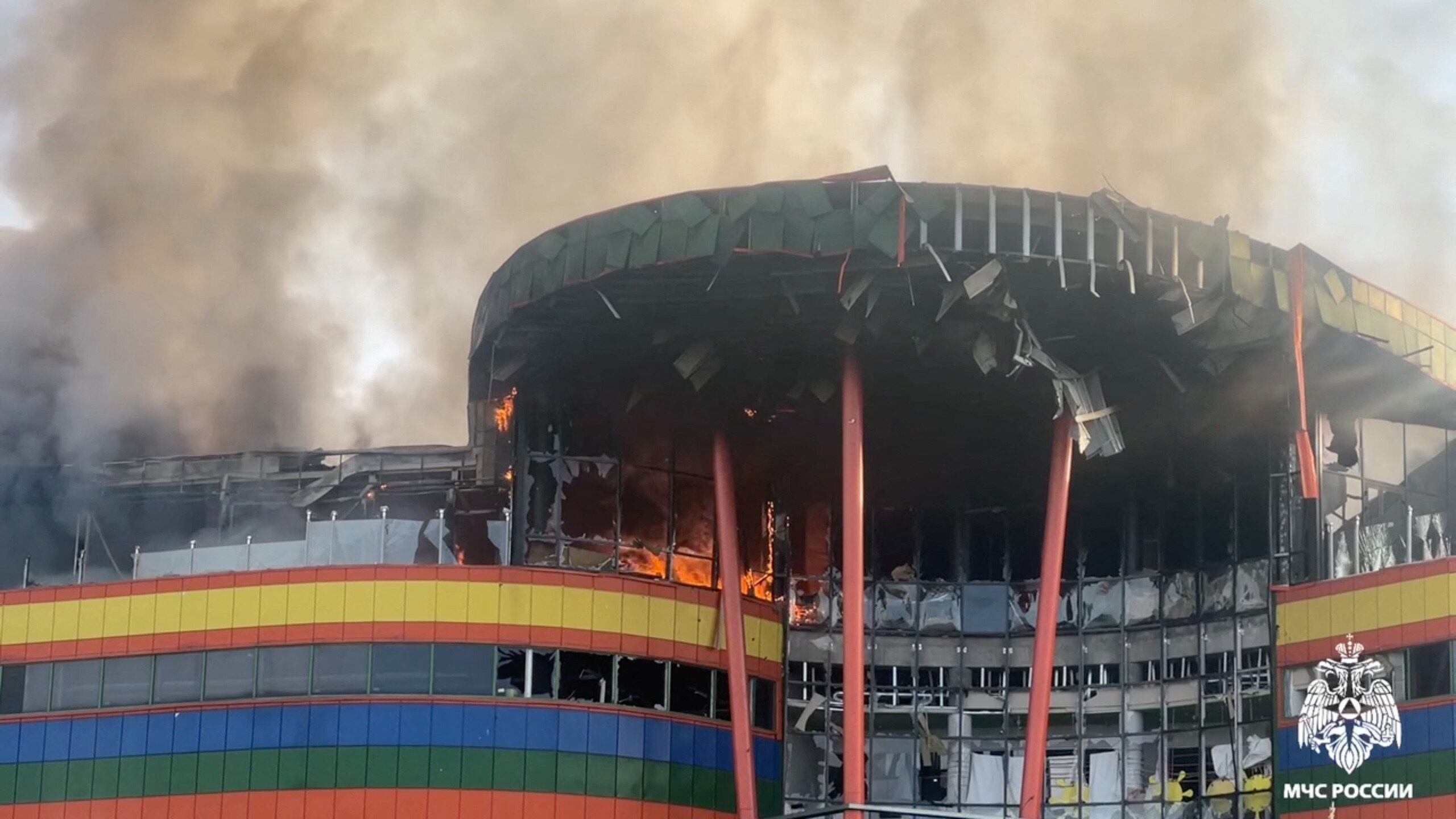 The facade of a shopping mall with its windows blown open, and smoke rising from it
