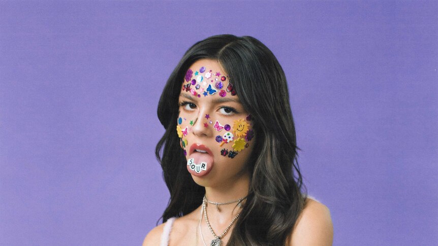 Photograph of Olivia Rodrigo sticking her tongue out with fun stickers all over her face.