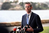 dominic perrottet speaking in front of microphones next to the waterfront