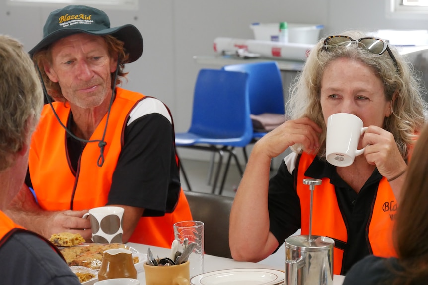 A man and a woman in orange vests drinking a mug of tea