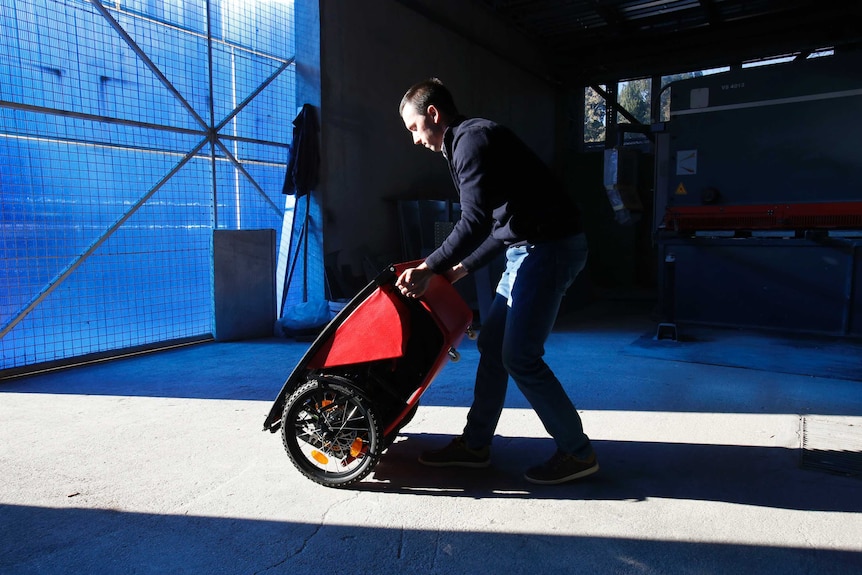 A man folds a small vehicle on the floor inside a warehouse.