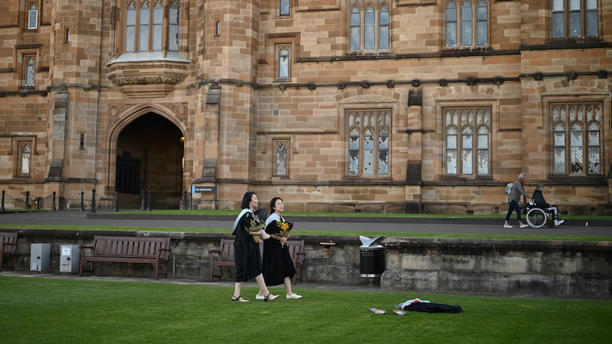 Two female graduates walk past Sydney University.