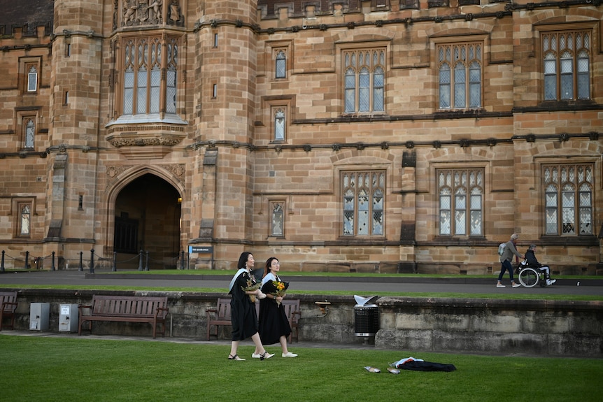 Two female graduates walk past Sydney University.