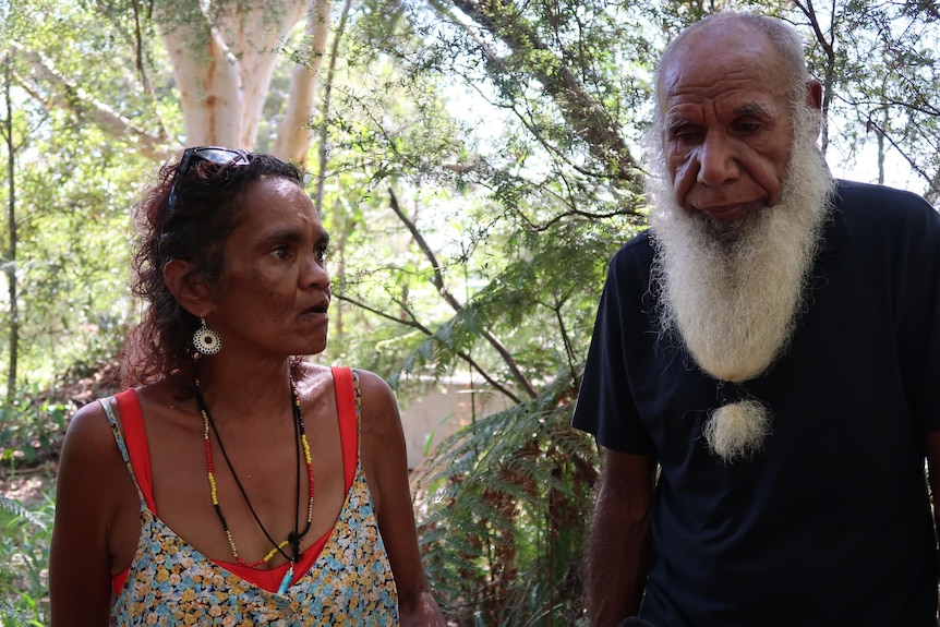 An indigenous woman and man converse inside bushland.