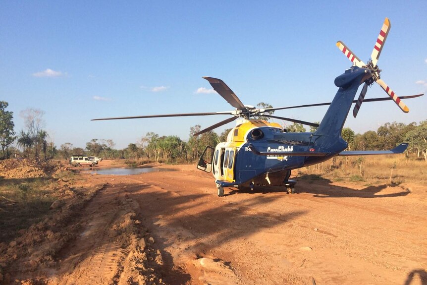 A blue, yellow and white CareFlight helicopter is seen after landing on a red dirt road.