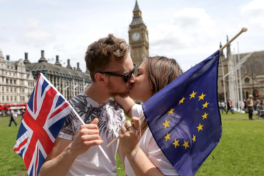 People kiss and hold small EU and Union flags in front of the Houses of Parliament in central London
