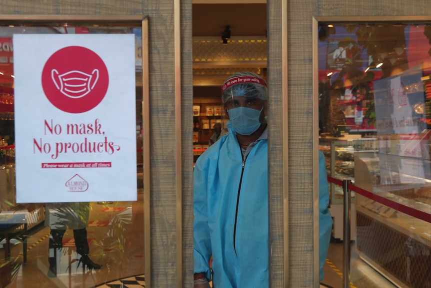 An Indian security personnel wearing protective gear stands by the entrance of a sweet shop in Hyderabad.