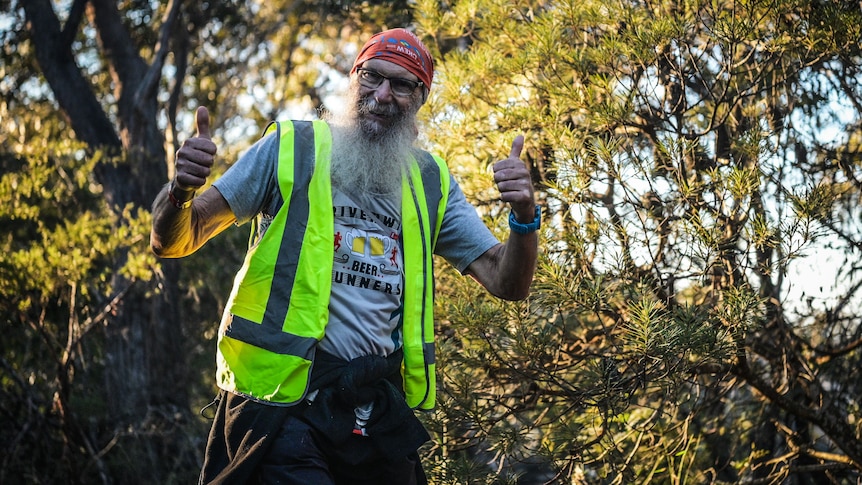 Man wearing high-vis jacket smiling with trees in the background.