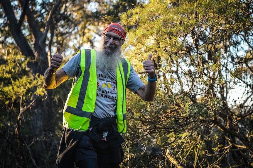 Man wearing high-vis jacket smiling with trees in the background.