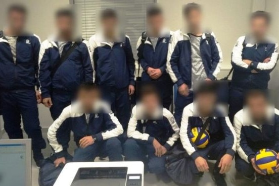 A group of ten males are grouped together, their faces are blurred and they are all wearing the same uniform.