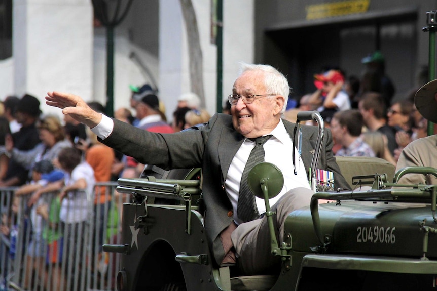A veteran taking part in the Brisbane Anzac Day march waves to the crowd from a jeep.