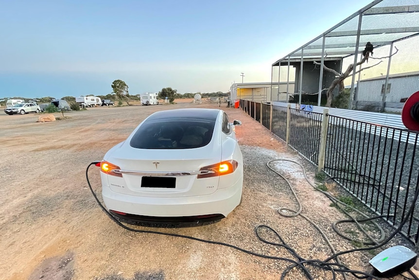 A shiny white car plugged into a wall with a desert in the background