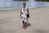 An older woman in a loose, sleeveless summer dress standing on a beach.