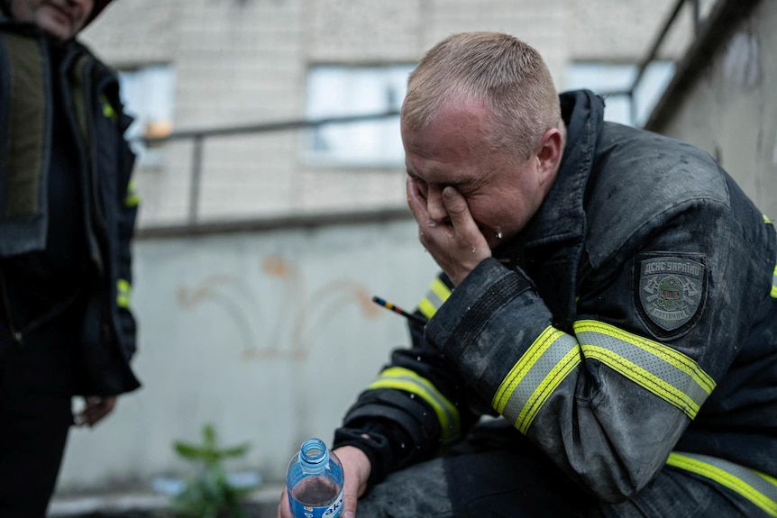 A rescuer holds his hand over his face and appears to be crying. 