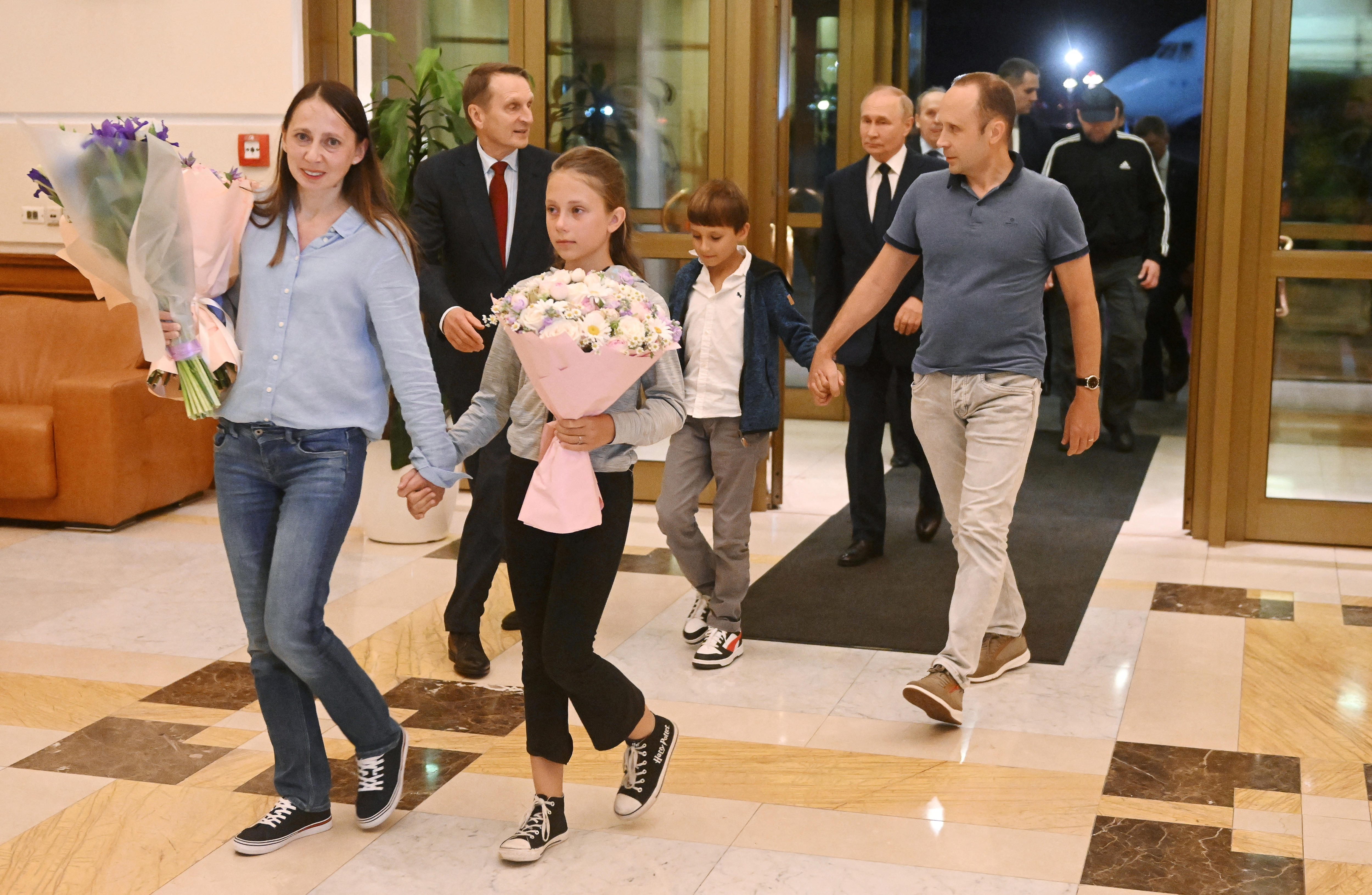 Dulsteva and her daughter walk into a lobby holding bouquets, with Dultsev and their son behind.