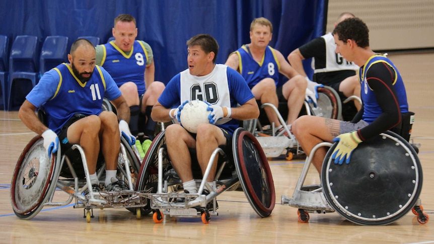 Wheelchair rugby players chase a ball.