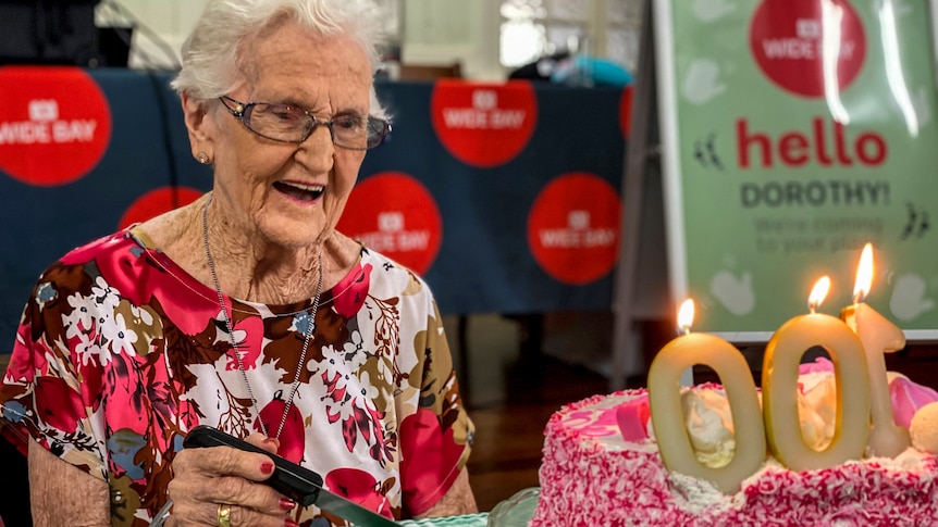 An elderly woman sits with a 100 birthday cake.