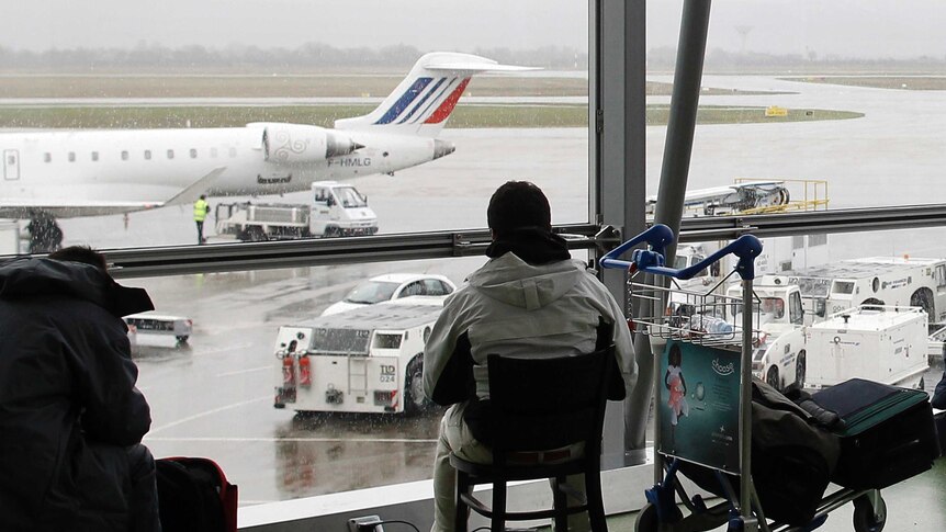 A passenger sits on a chair looking through the window as he waits for his flight