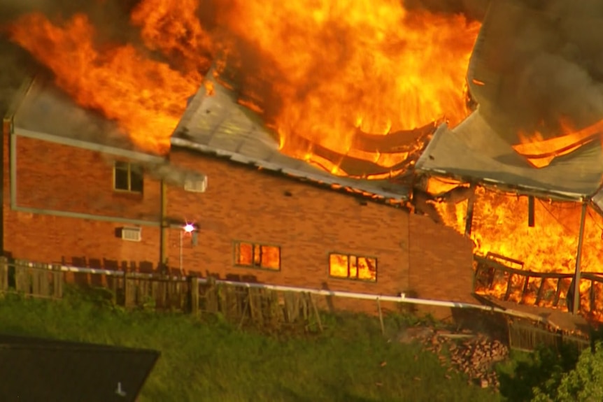 A brick building with bright orange flames streaming out from its roof